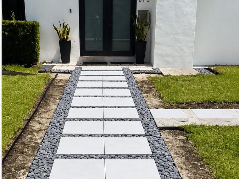 After: the same entrance with a run of white paver slabs set in black river rock, leading to the same black french doors.
