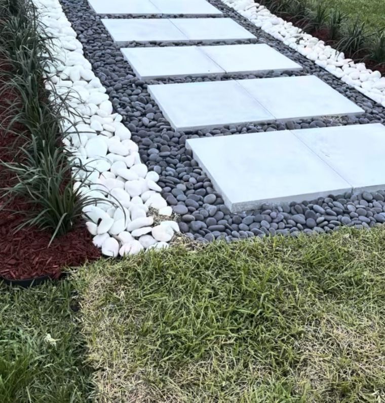 Finished paver walkway with black river rock border and a red mulch bed with variegated grasses.