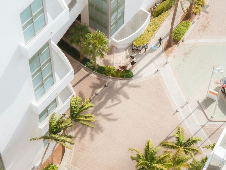 Courtyard of a white residential building framed by palms, shaped hedges and paver walkways.