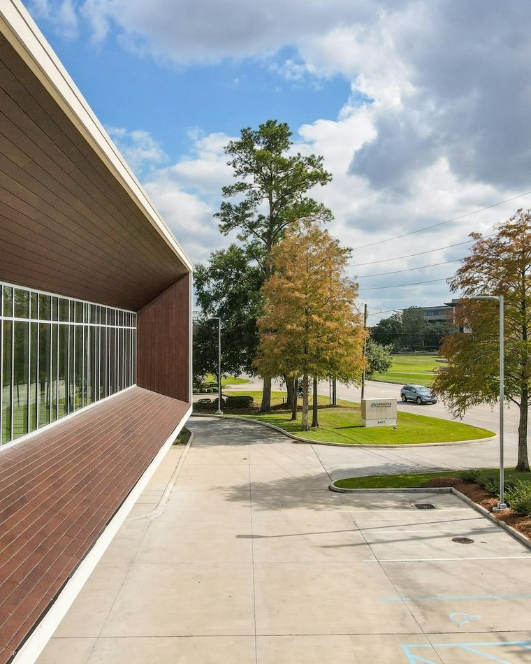 Mature trees and trimmed planting beds framing the walkway of a commercial building.