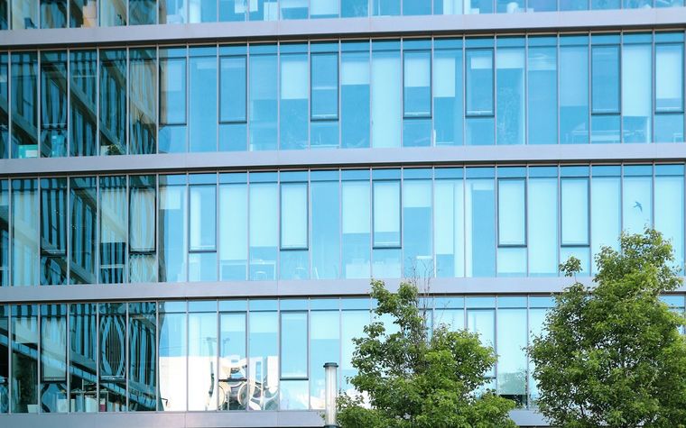 Office building with a maintained lawn, clipped hedges, and planted beds along the entrance.